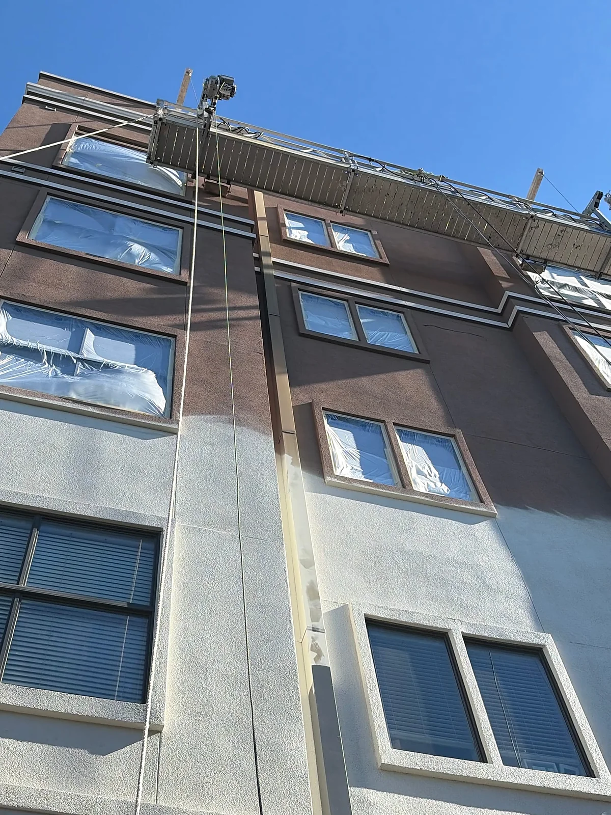 Masked windows and a suspended work platform on a multistory facade during exterior painting in Dallas.