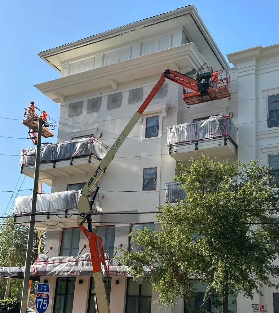 Workers using lifts alongside a multifamily facade with patched surfaces and covered balconies