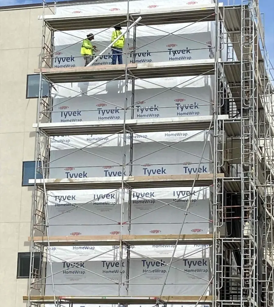 Crew installing building wrap behind scaffolding on an exterior wall