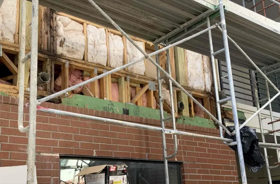 Exposed wall framing and insulation above a brick facade during water intrusion repairs