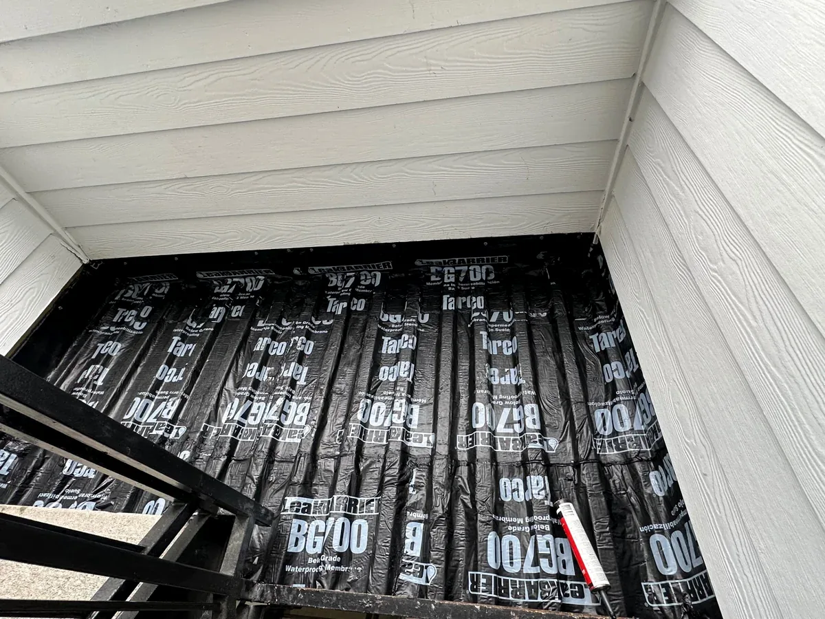Membrane across an apartment landing beside siding and a metal railing in Urbana, Illinois.