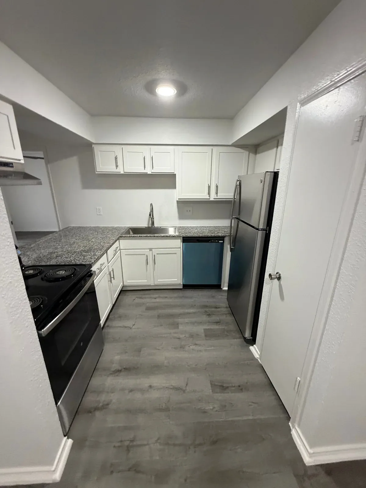 Apartment kitchen in Austin with white cabinetry, countertop, appliances, and plank flooring