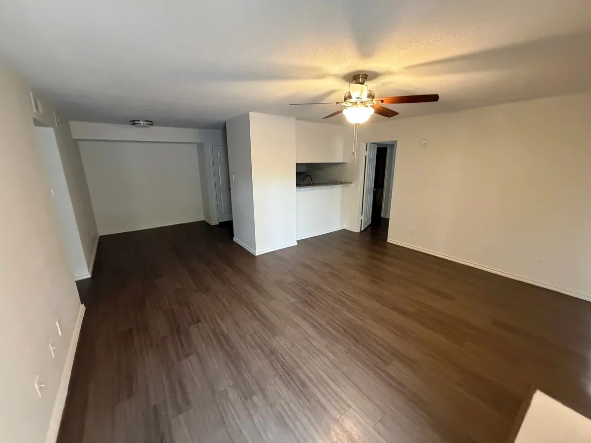 Empty apartment living area in Austin with plank flooring, a ceiling fan and a kitchen pass-through.