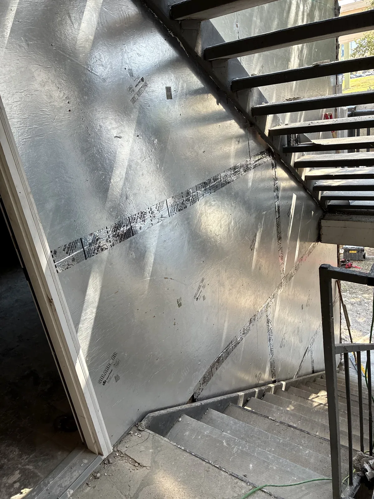 Foil-faced wall panels and taped seams beside an exterior stair during Dallas reconstruction work.