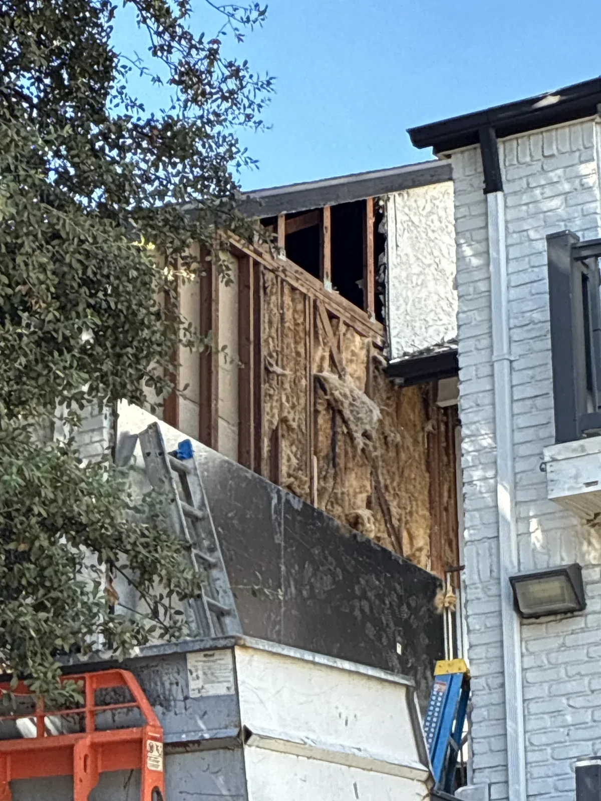 Exposed wall framing and insulation beside an apartment balcony during restoration work in Dallas.