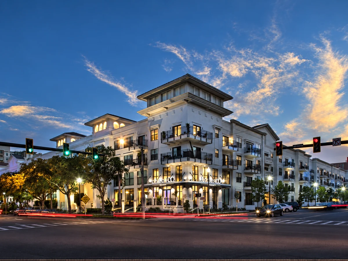 Multifamily building exterior at dusk with illuminated windows and street-level commercial space